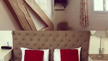 Une chambre à coucher avec un grand lit, une poutre en bois au plafond, un téléviseur et une fenêtre avec des rideaux.
