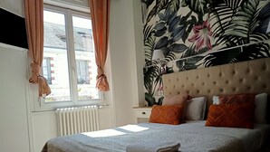 Een slaapkamer met een bed, een raam met gordijnen, een radiator en een wand met tropische behang.