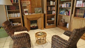 Een gezellig leeshoekje met rieten stoelen, een klein rond tafeltje en boekenplanken vol boeken en ingekaderde foto's.