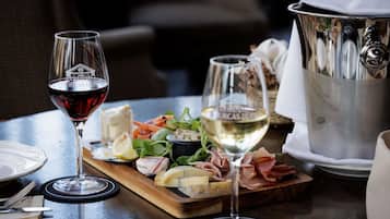 A dining table with a wine glass, a cheese board with various cheeses and meats, a pitcher, and a bottle of white wine.