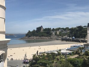 Un pueblo costero con una playa arenosa, un faro y una colina con edificios.