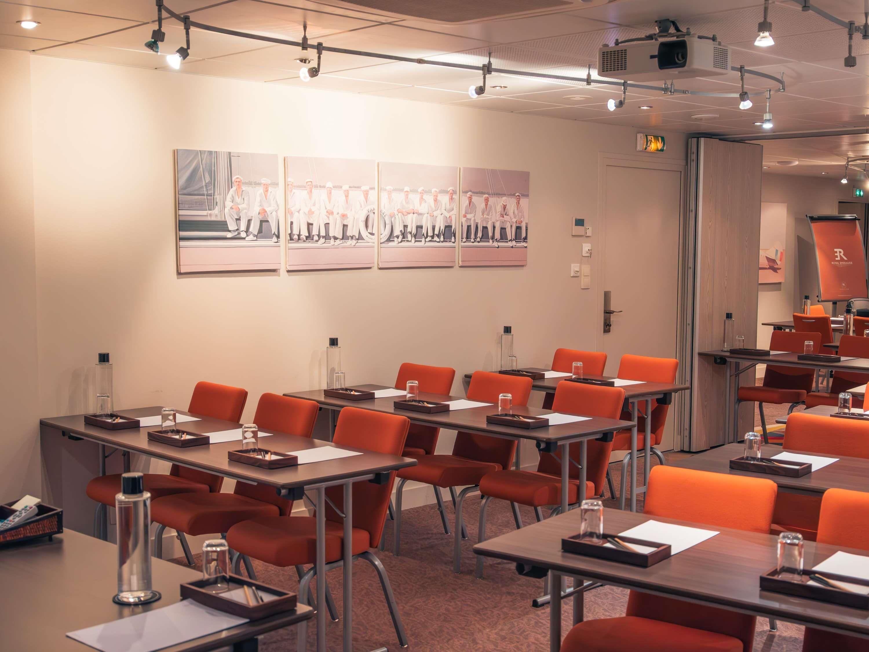 Un salón de conferencias con mesas, sillas y una pantalla para proyector.