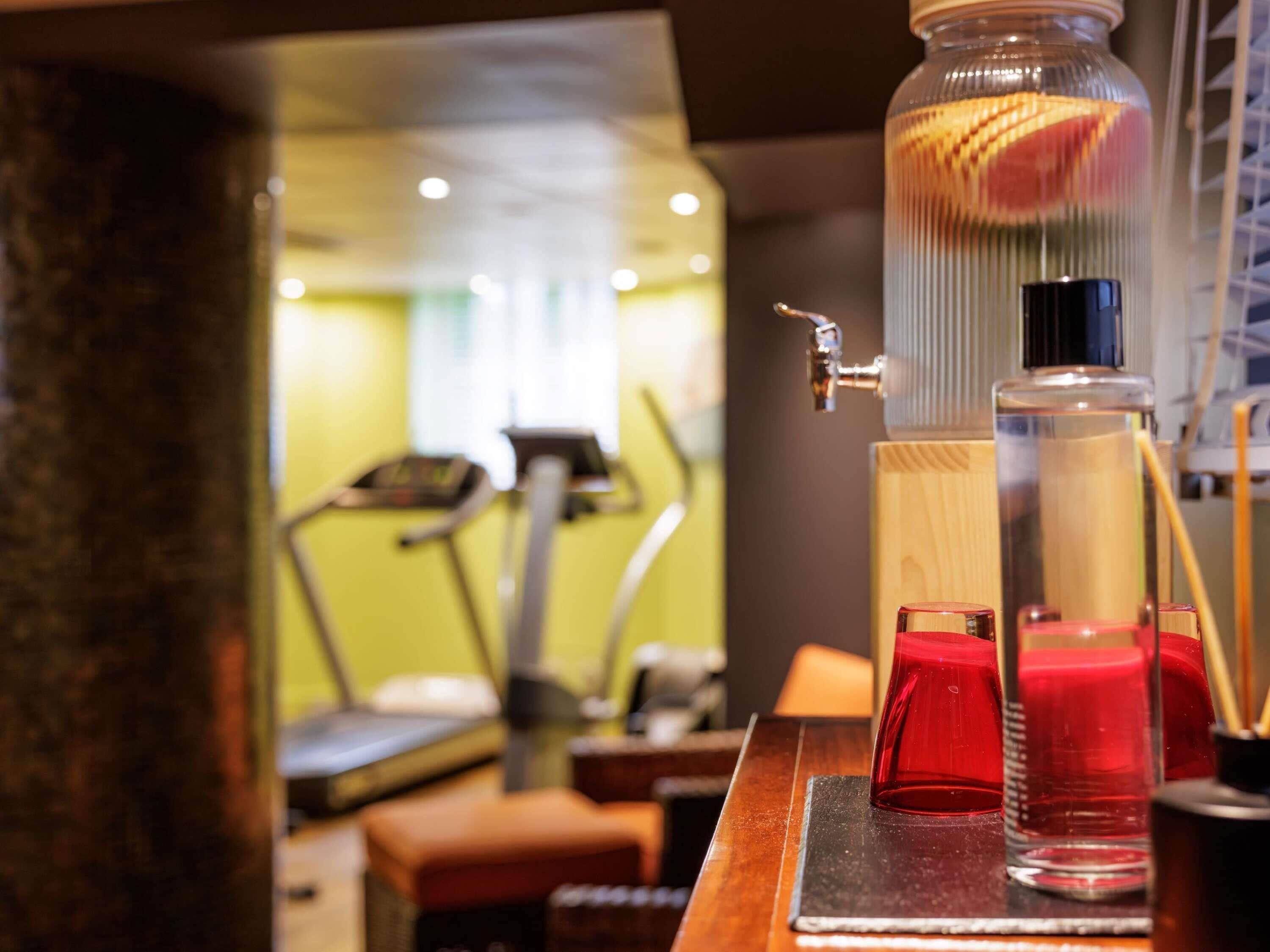 A bar area with a water dispenser, glasses, and a treadmill in the background.