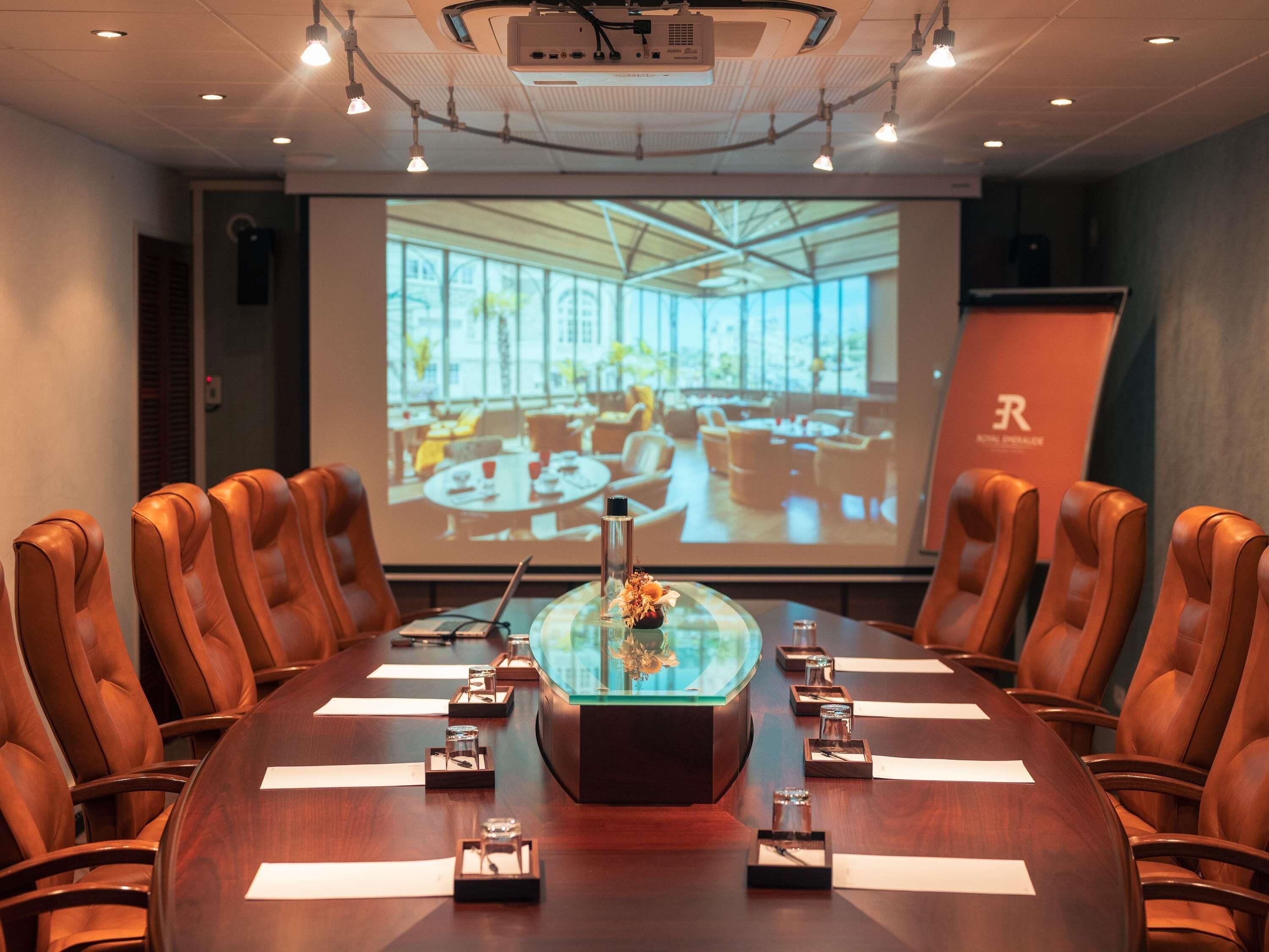 Une salle de conférence avec une longue table, des fauteuils en cuir, un écran de projection et une vitrine.