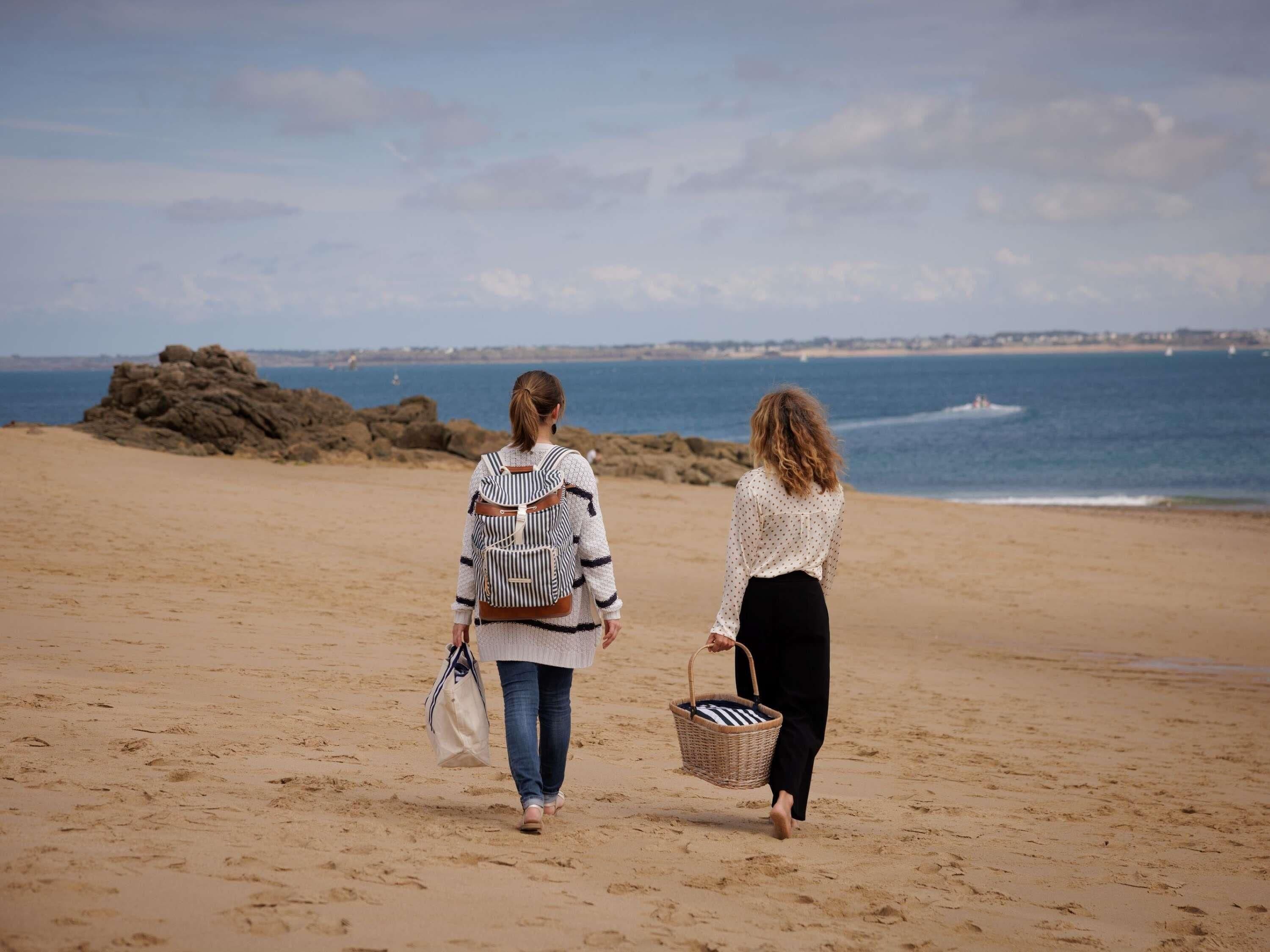 Two people walking on a sandy beach with a rocky outcrop and the sea in the background.
