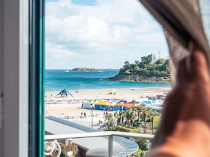 Une vue sur la côte, avec une plage, des parasols et un bâtiment situé sur une colline.
