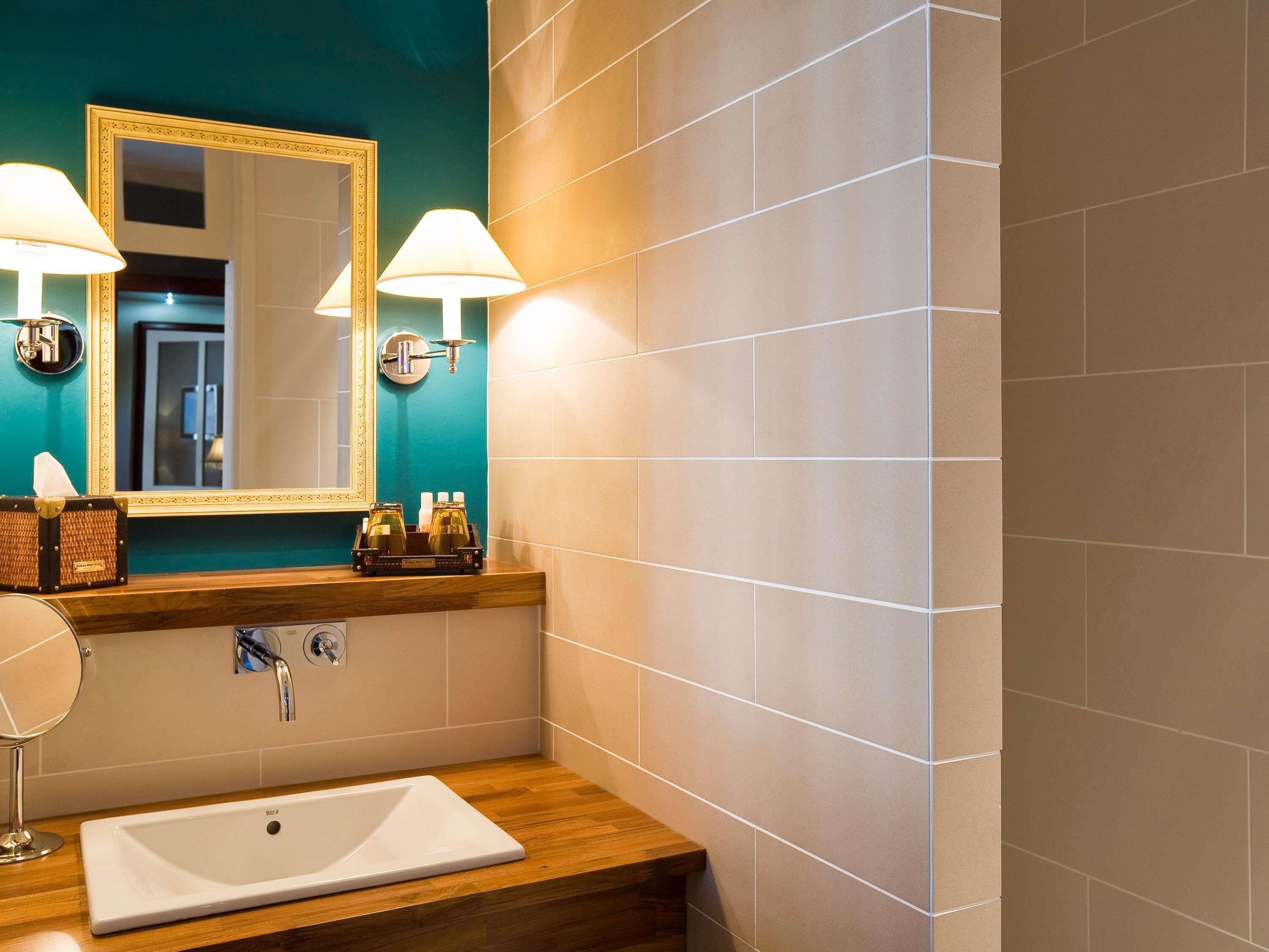 A bathroom with a white sink, two wall-mounted lamps, a mirror with a gold frame, and a teal accent wall.