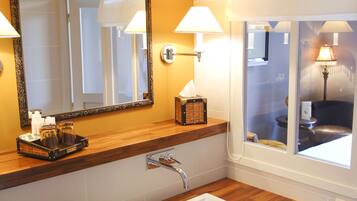 A bathroom with a wooden vanity, a white sink, a mirror with an ornate frame, and two wall-mounted lamps.