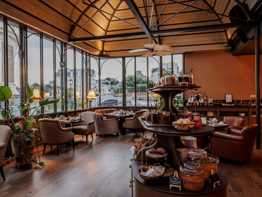 A spacious room with a high ceiling, large windows, and a central serving area with food and drink options.