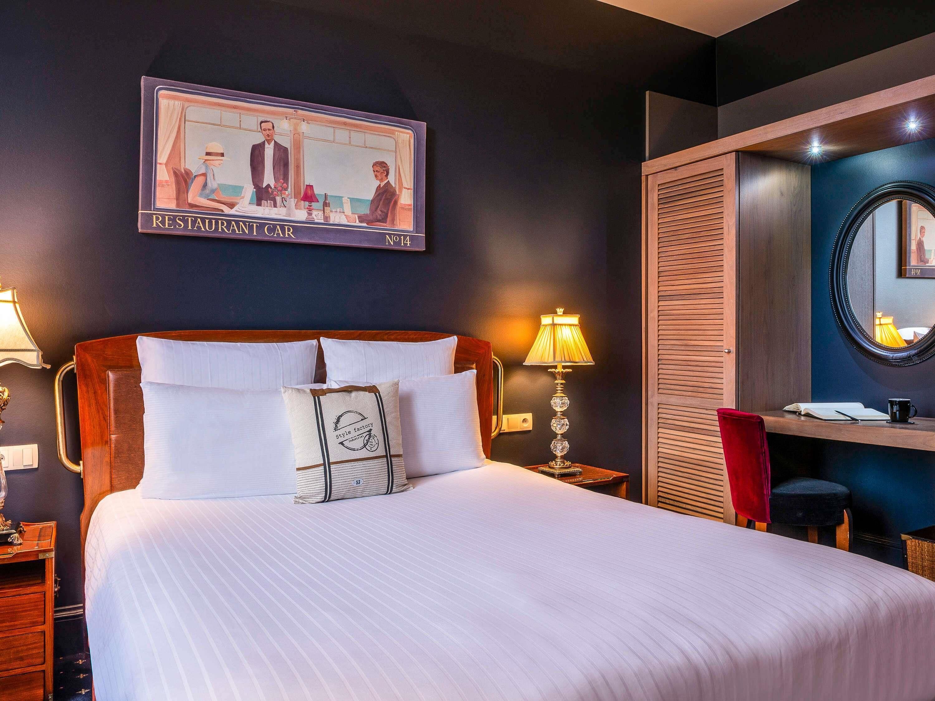 Ein Hotelzimmer mit einem Bett, einem Schreibtisch, einem Stuhl, einer Lampe, einem Spiegel und einem Bild an der Wand.