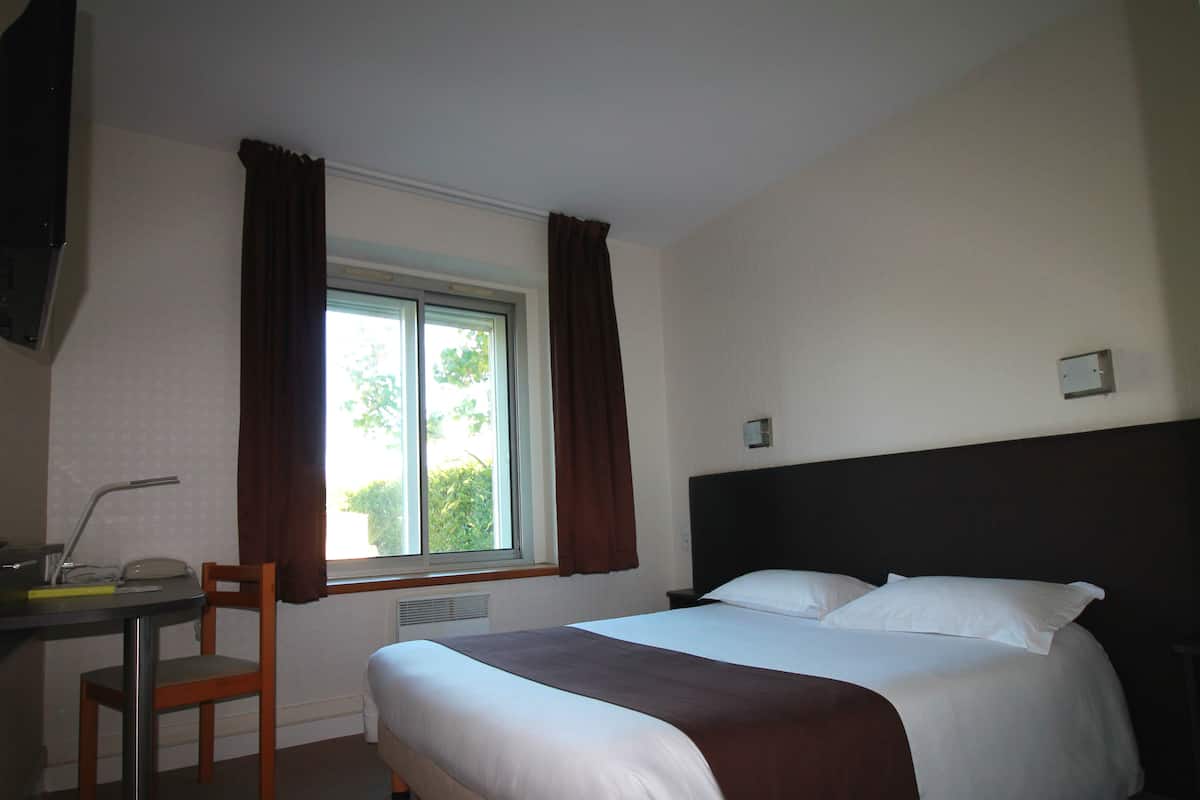 A hotel room with a bed, a desk, a chair, and a window with curtains.