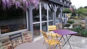 Een buitenruimte met een tafel en stoelen, een stenen muur en een glazen deur die naar een auto leidt.