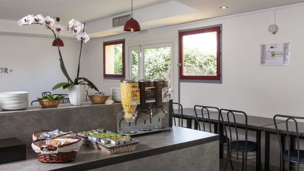 A modern kitchen with a central island, a dining area with chairs, and a window with a view of greenery. - Hotel & Residence Calais Car Ferry (Calais)
