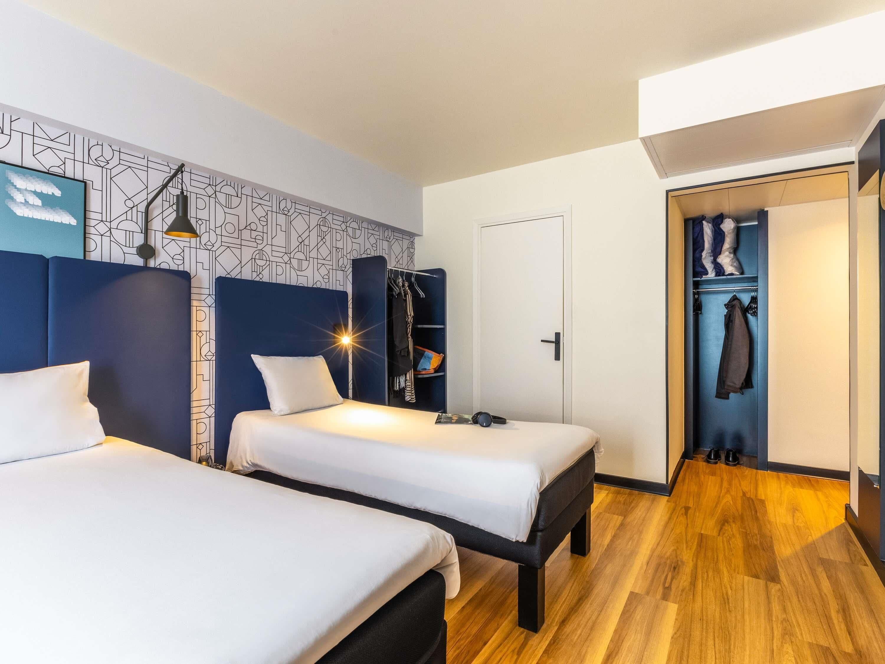 Een moderne hotelkamer met twee bedden, een garderobe en een kapstok.