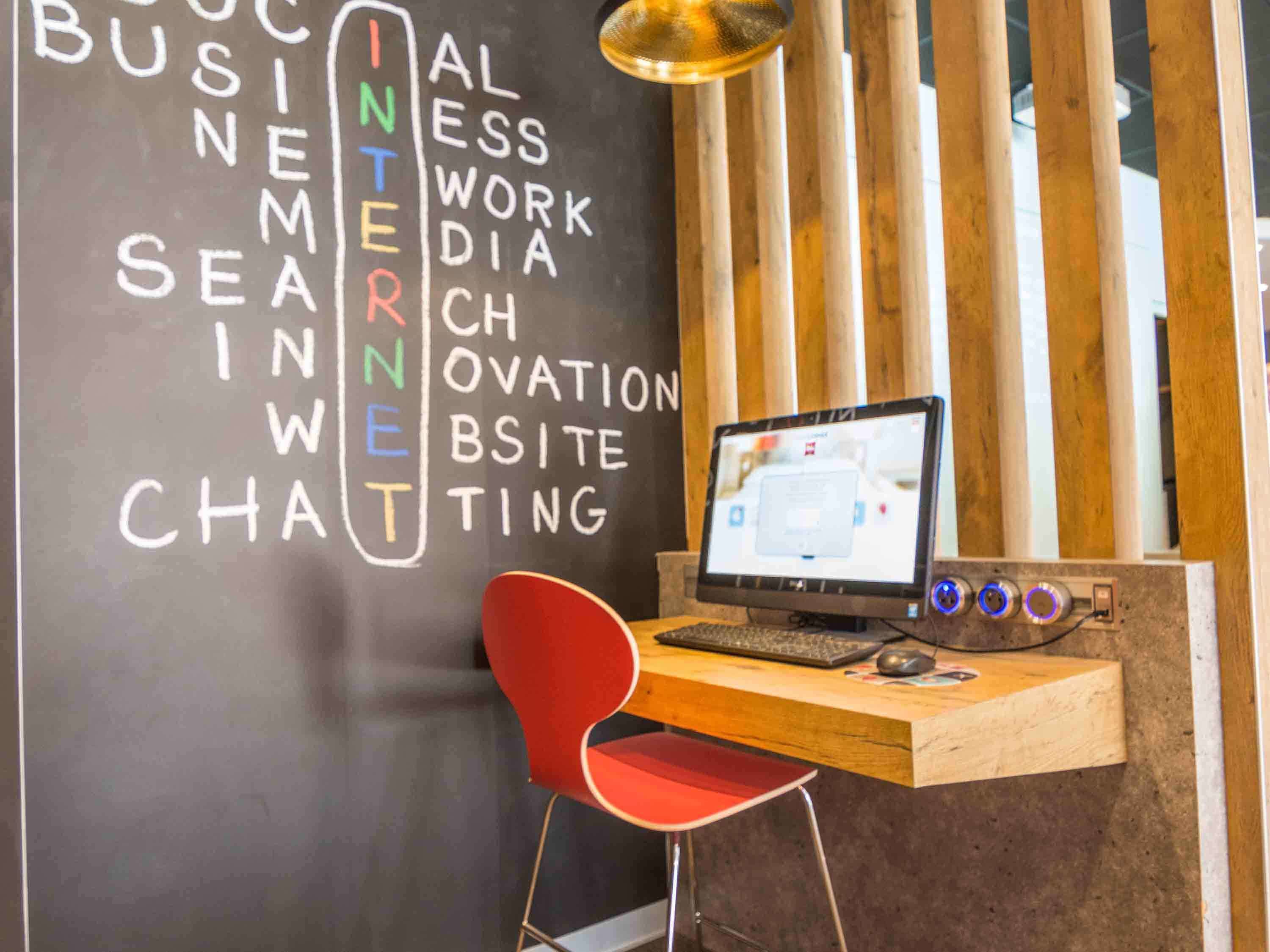 Un espacio de trabajo con una computadora portátil sobre un escritorio de madera, una silla roja y una pared con palabras relacionadas con internet y negocios.