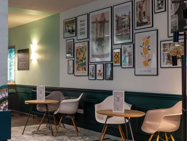 A cafe with a wall adorned with various framed artworks and a seating area with two round tables and four chairs.