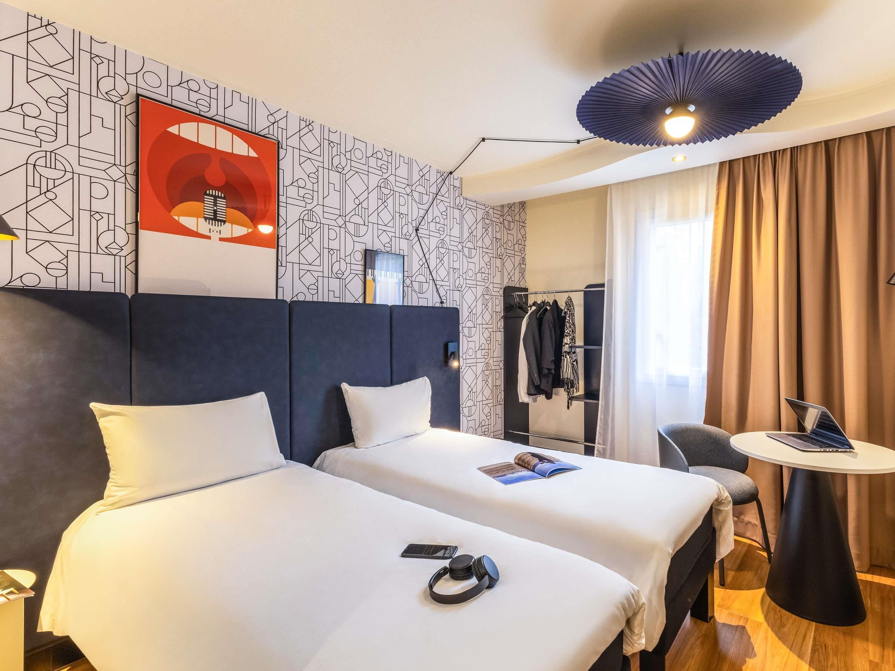 A hotel room with two beds, a desk, a chair, a ceiling fan, and a patterned wall.