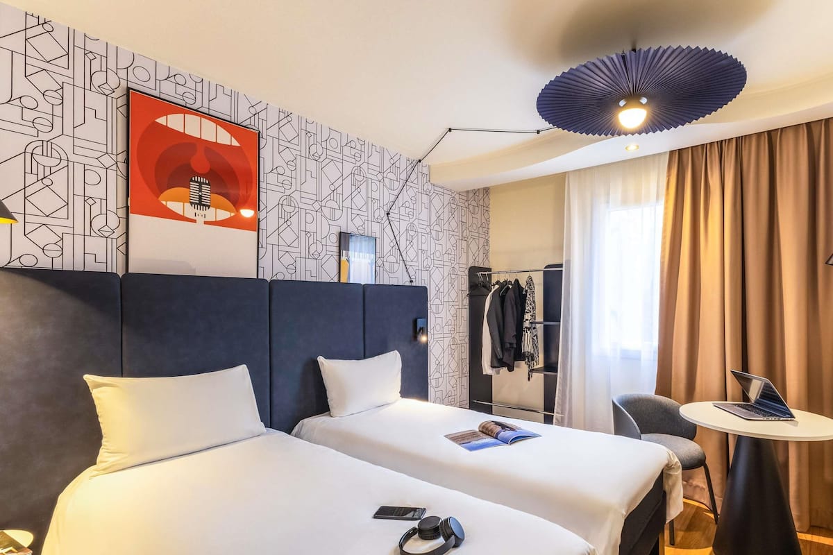 A hotel room with two beds, a desk, a chair, a ceiling fan, and a patterned wall.