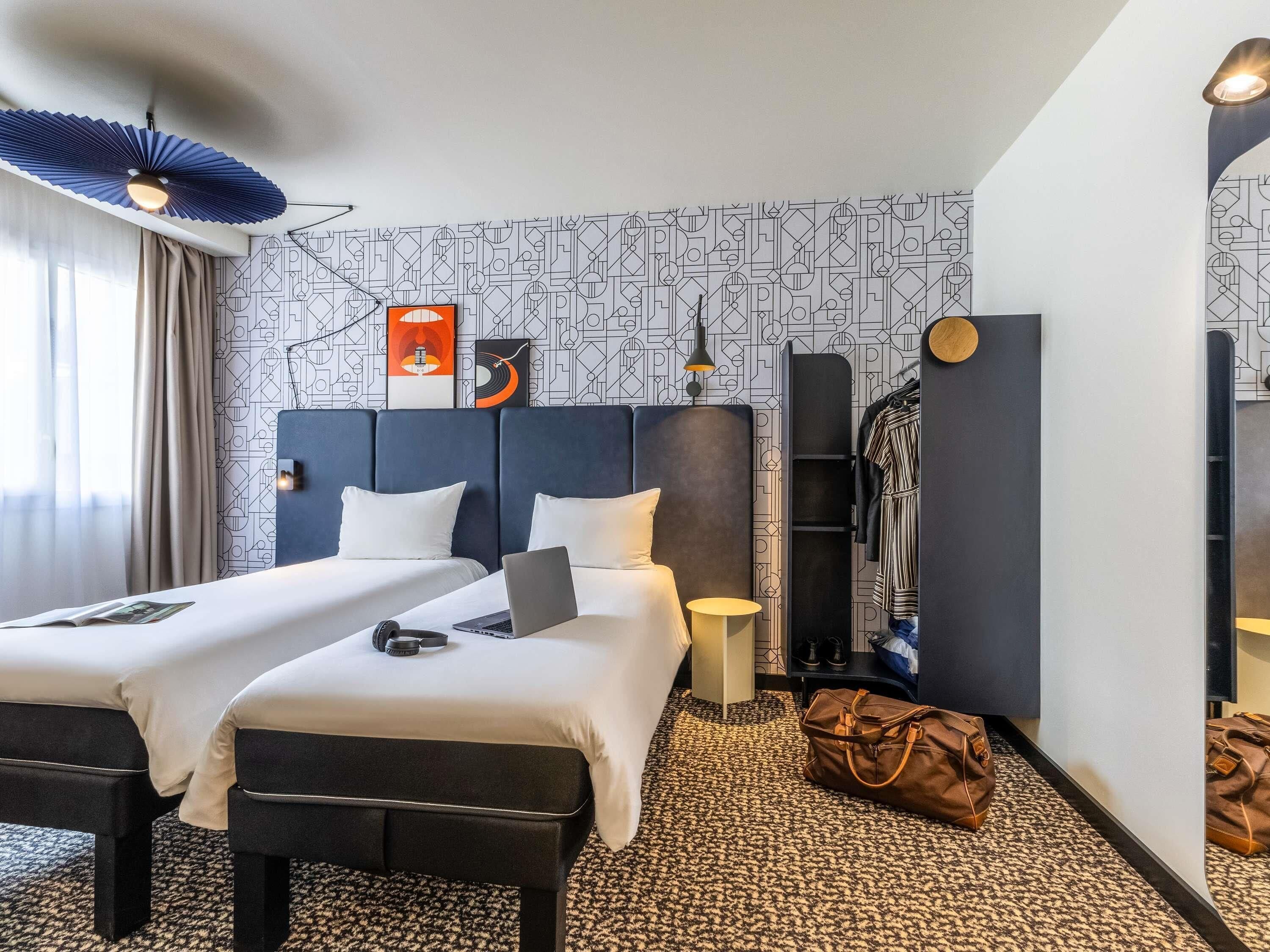 A hotel room with two beds, a desk, a laptop, a handbag, and a coat rack.
