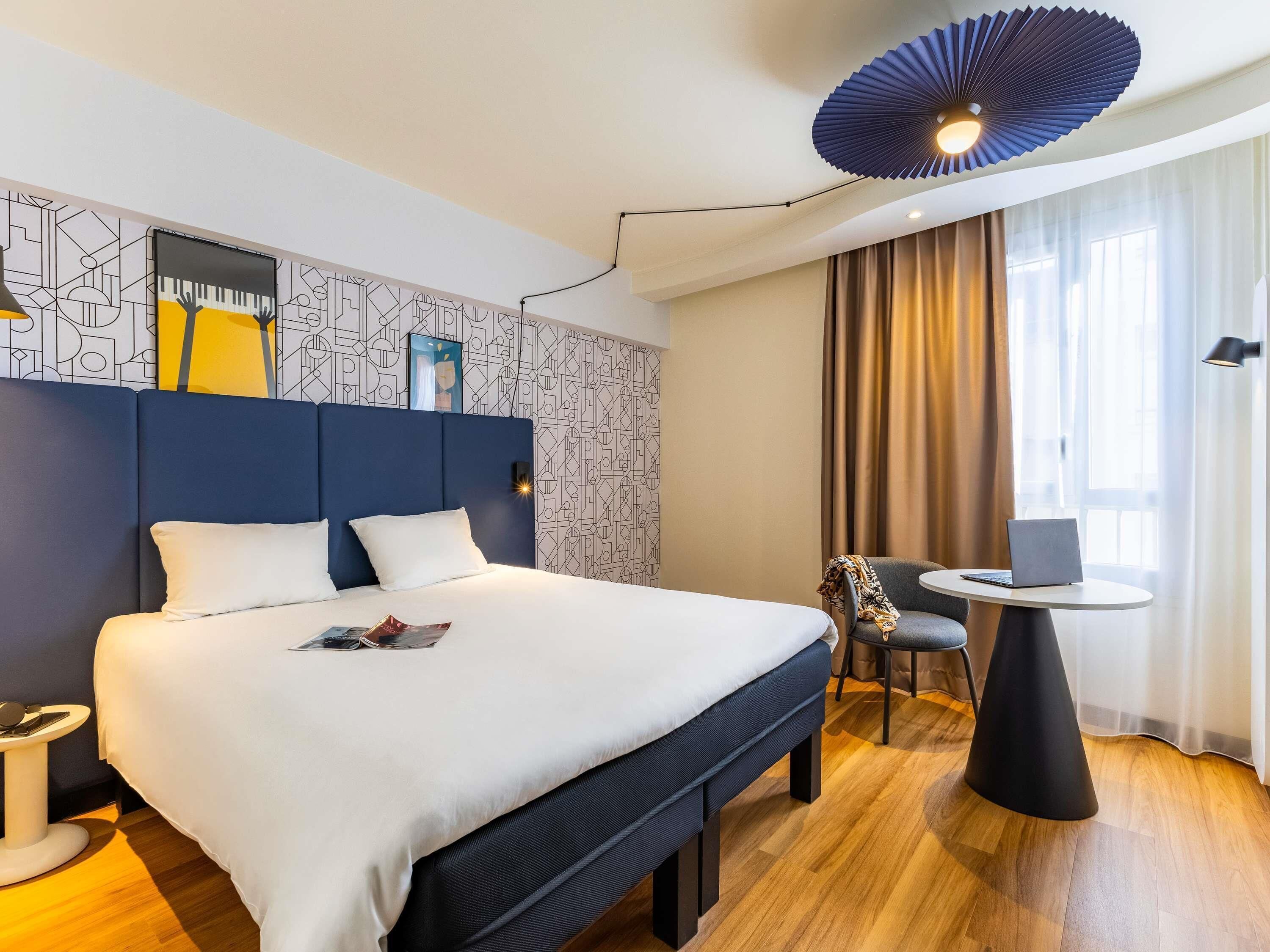 Quarto de hotel moderno com uma cama grande, uma mesa redonda pequena e uma cadeira.