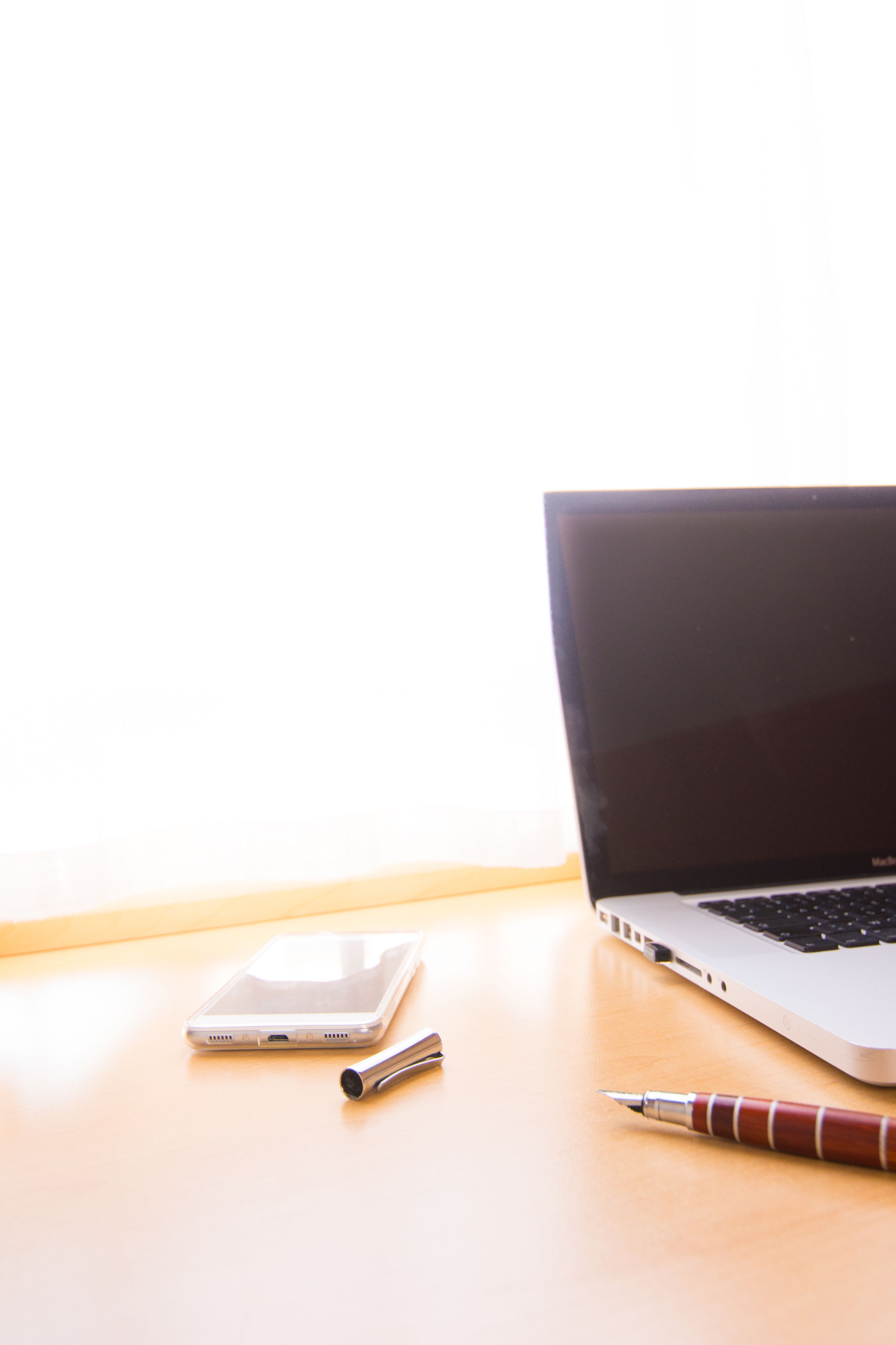 A laptop, a smartphone, and a pen on a wooden surface.