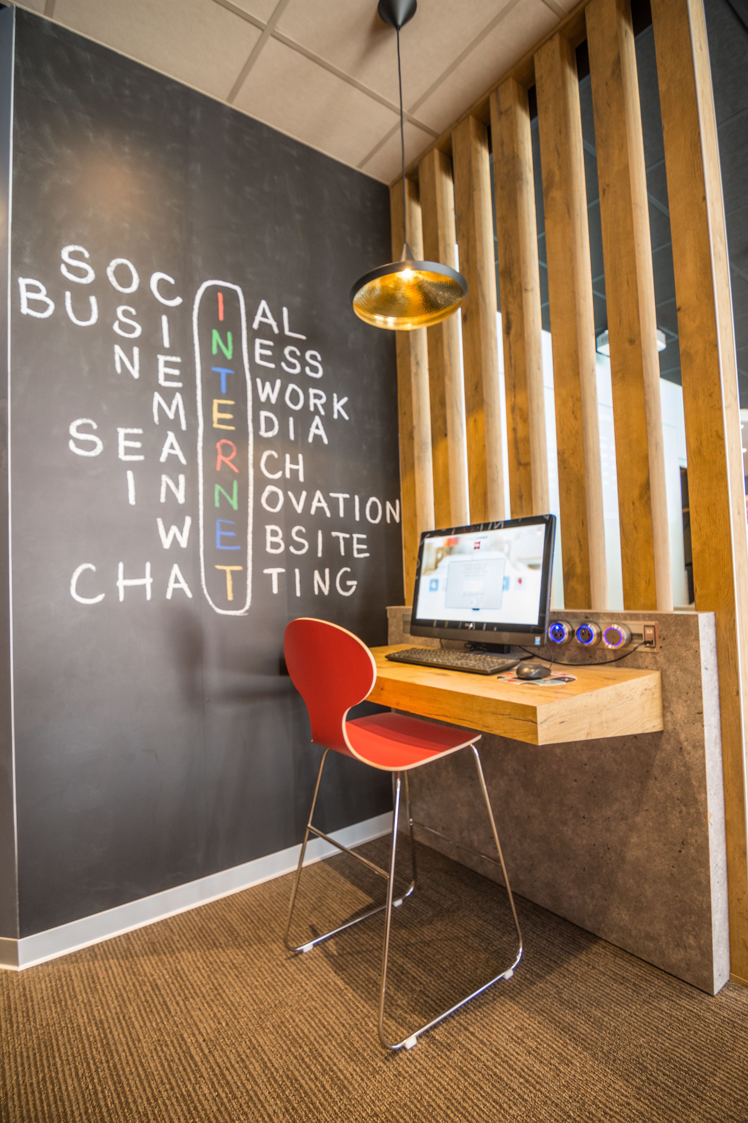 Un espace de travail comprenant un bureau, un ordinateur et une chaise rouge. Le mur est décoré de texte et de lambris en bois.