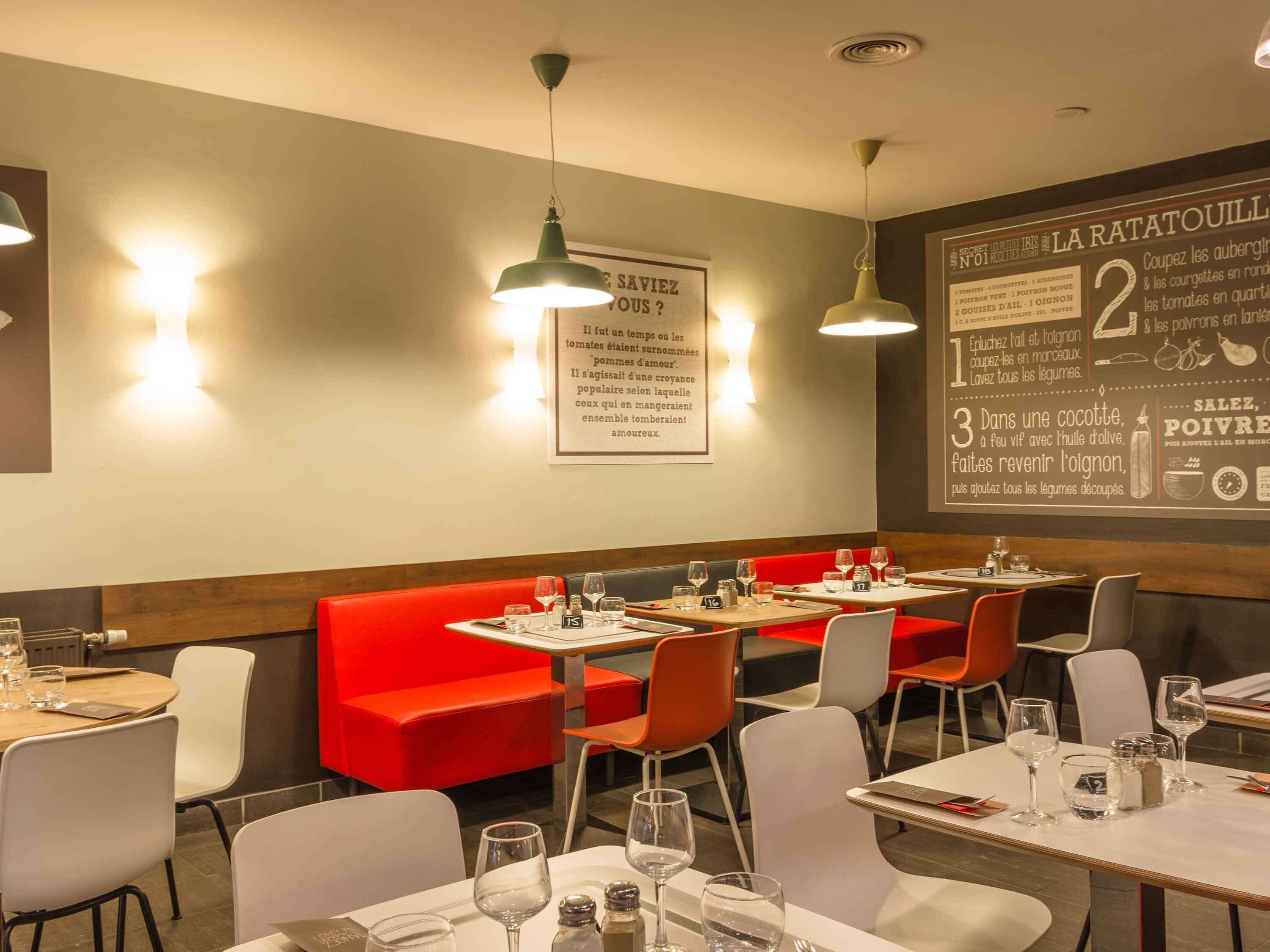 A restaurant interior with red seating, white tables, and pendant lighting.