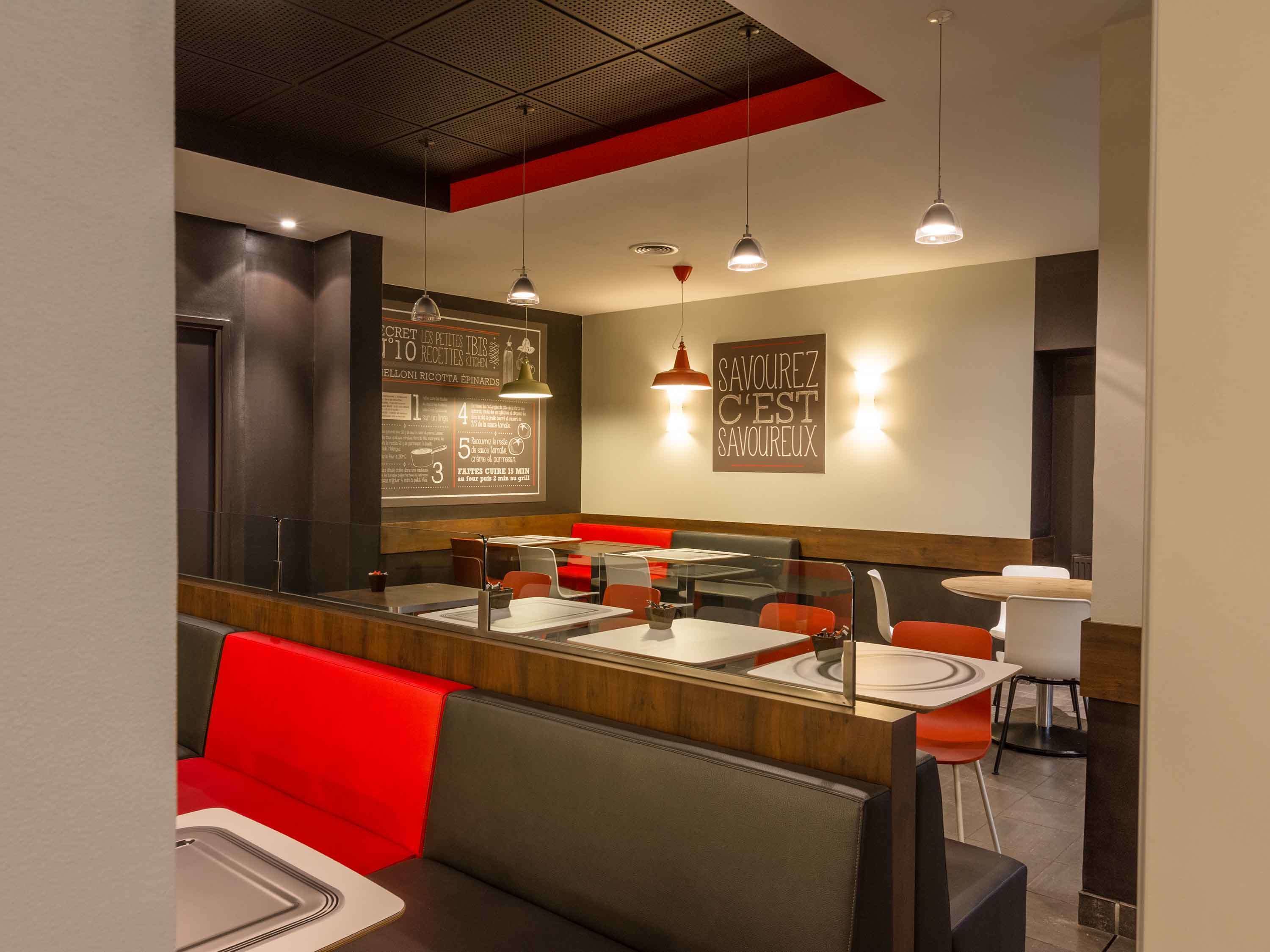 A modern restaurant interior with red and grey seating, pendant lighting, and a chalkboard menu.