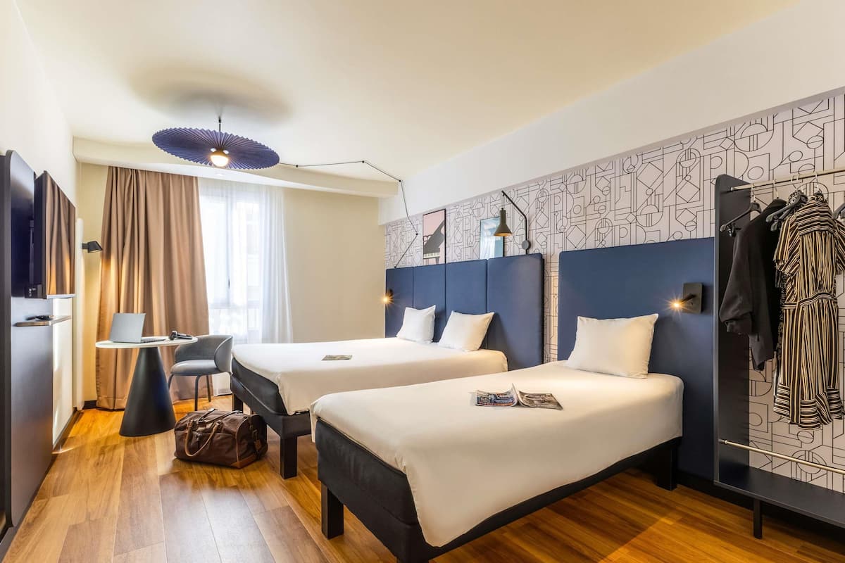 Habitación de hotel con dos camas, un escritorio, una silla, un armario y una pared con diseño.
