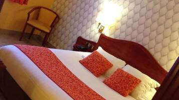 Una habitación de hotel con cama, una silla, una lámpara de pared y un cabecero estampado.