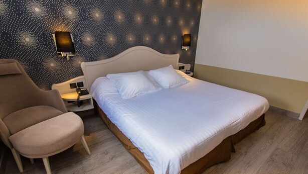 A neatly made bed with white linens, a wooden headboard, and two wall-mounted nightstands with lamps. - Citotel Le Cedre (Noyon)