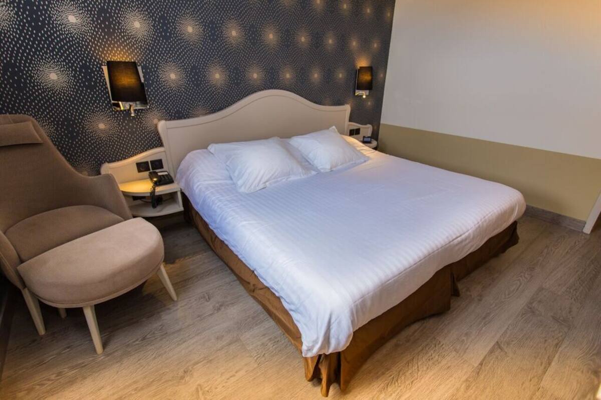 A neatly made bed with white linens, a wooden headboard, and two wall-mounted nightstands with lamps.