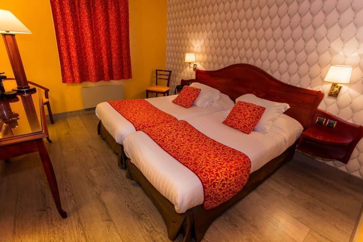 A hotel room with a large bed, two bedside tables, a chair, and a red curtain.