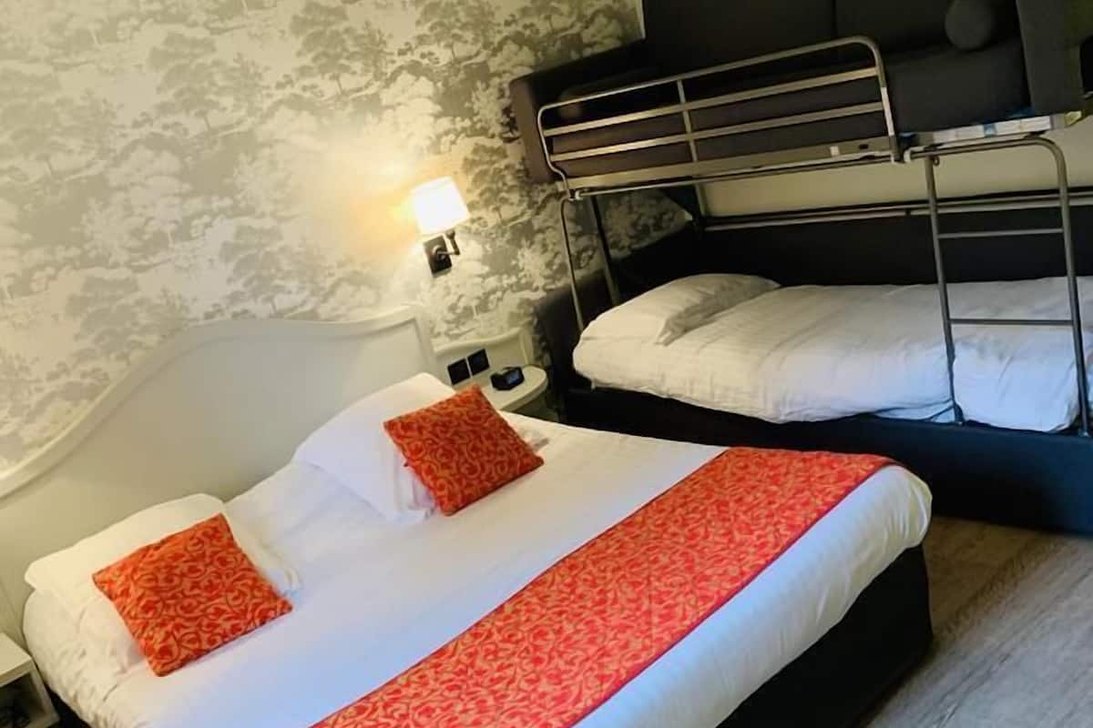 A room with a bunk bed, a single bed, and a nightstand with a lamp.