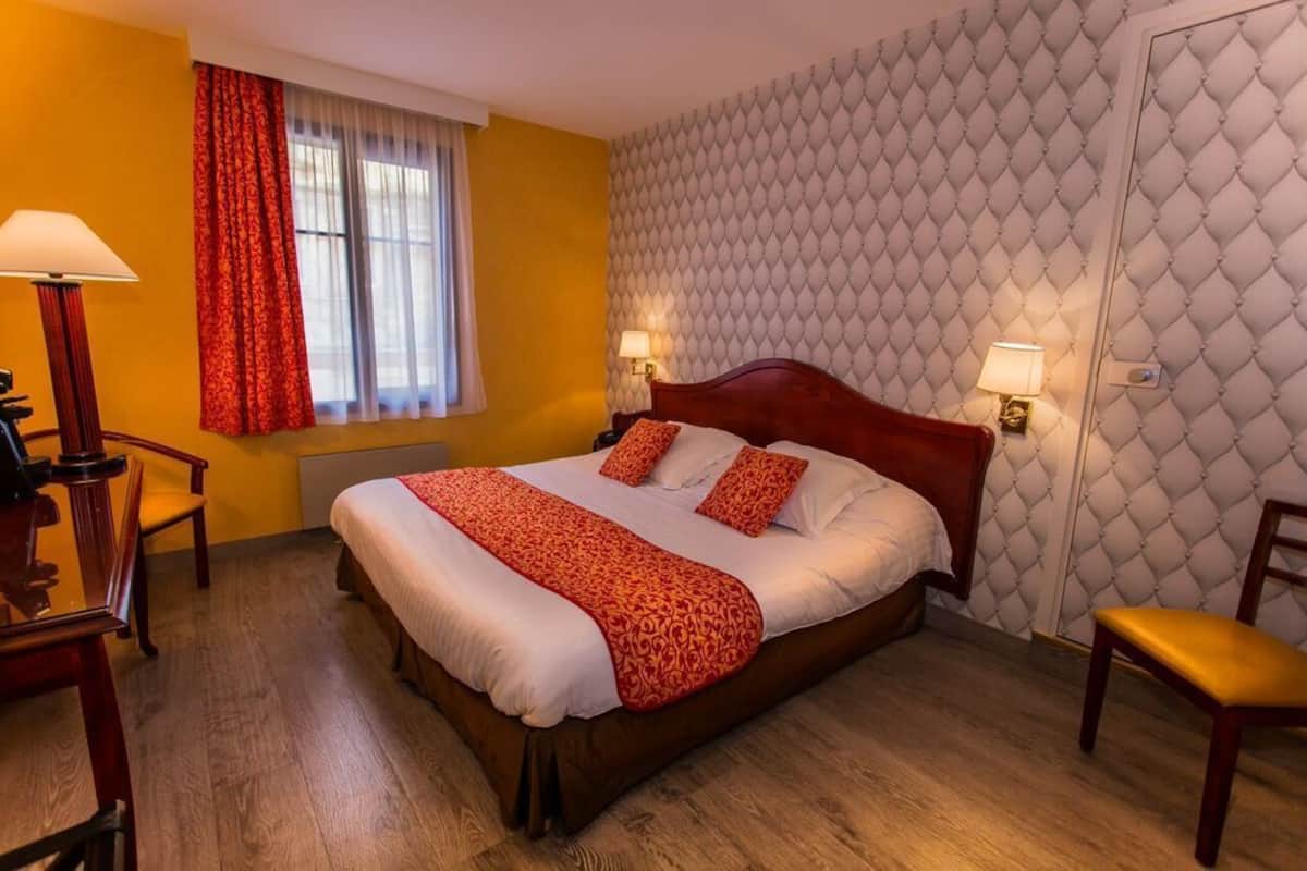 A hotel room with a large bed, two bedside lamps, a wooden desk, and a chair.