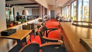 Un espace de restauration moderne, doté de hauts plafonds, de grandes fenêtres et d’une moquette rouge.