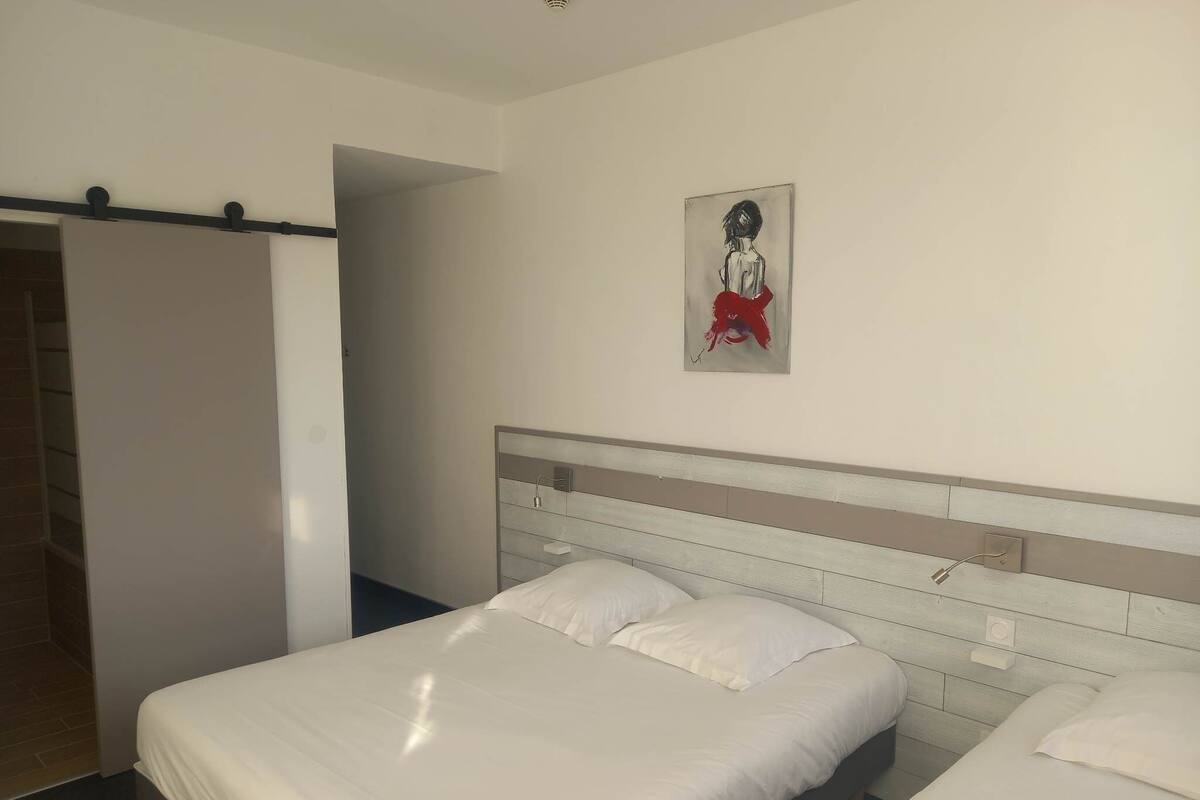 Une chambre d’hôtel avec deux lits, une tête de lit blanche, un tableau au mur et une porte donnant sur une autre pièce.