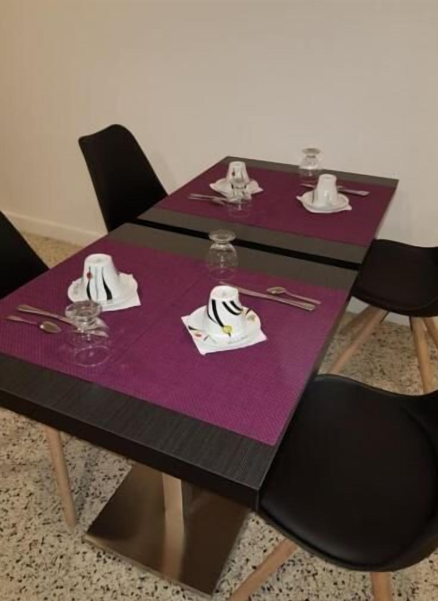 Una mesa de comedor dispuesta con servilletas blancas, cubiertos y vasos, rodeada de sillas negras.