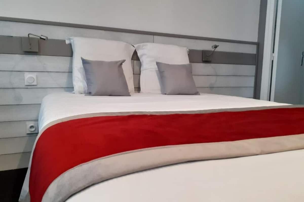 Un lit avec une couvre-lit rouge et blanche, deux oreillers et une tête de lit dotée d’un interrupteur.