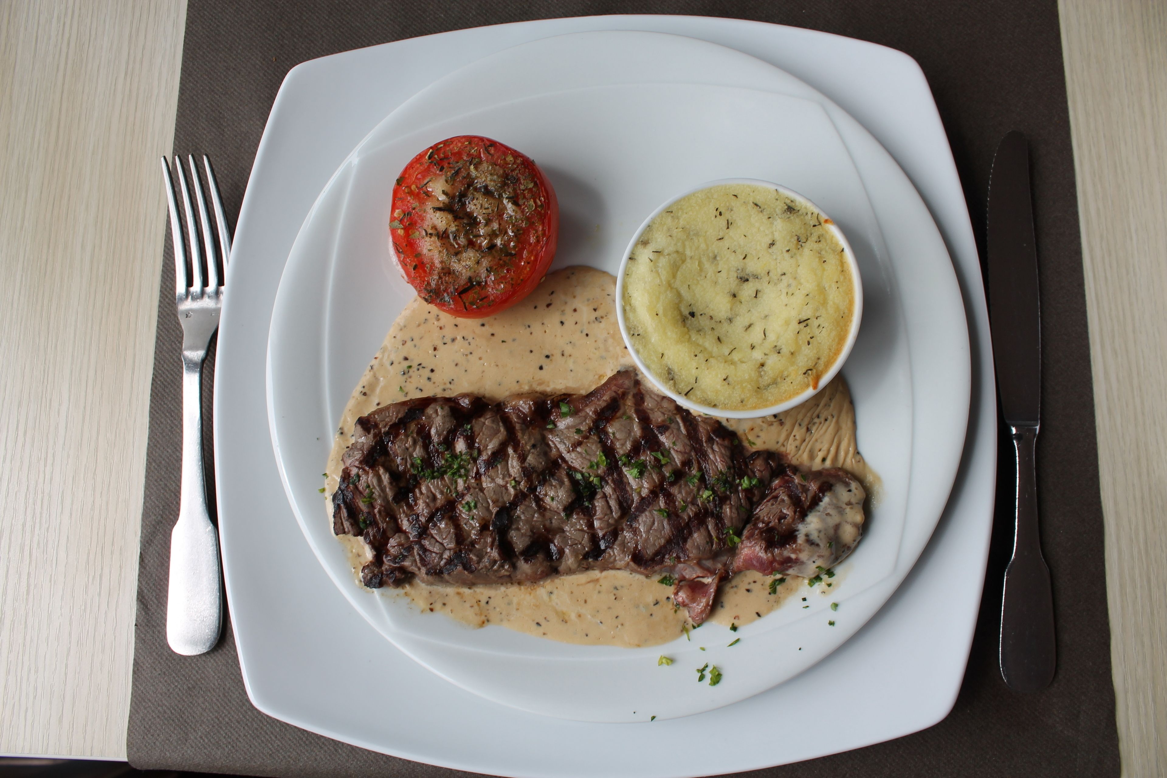 Un plato con un bistec, un tomate y puré de papas.