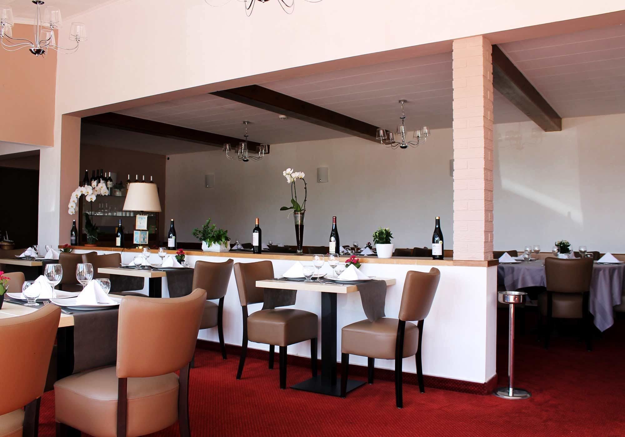 Een restaurant met gedekte tafels, een bar en een rode tapijtvloer.