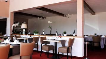 Een restaurant met gedekte tafels, een bar en een rode tapijtvloer.
