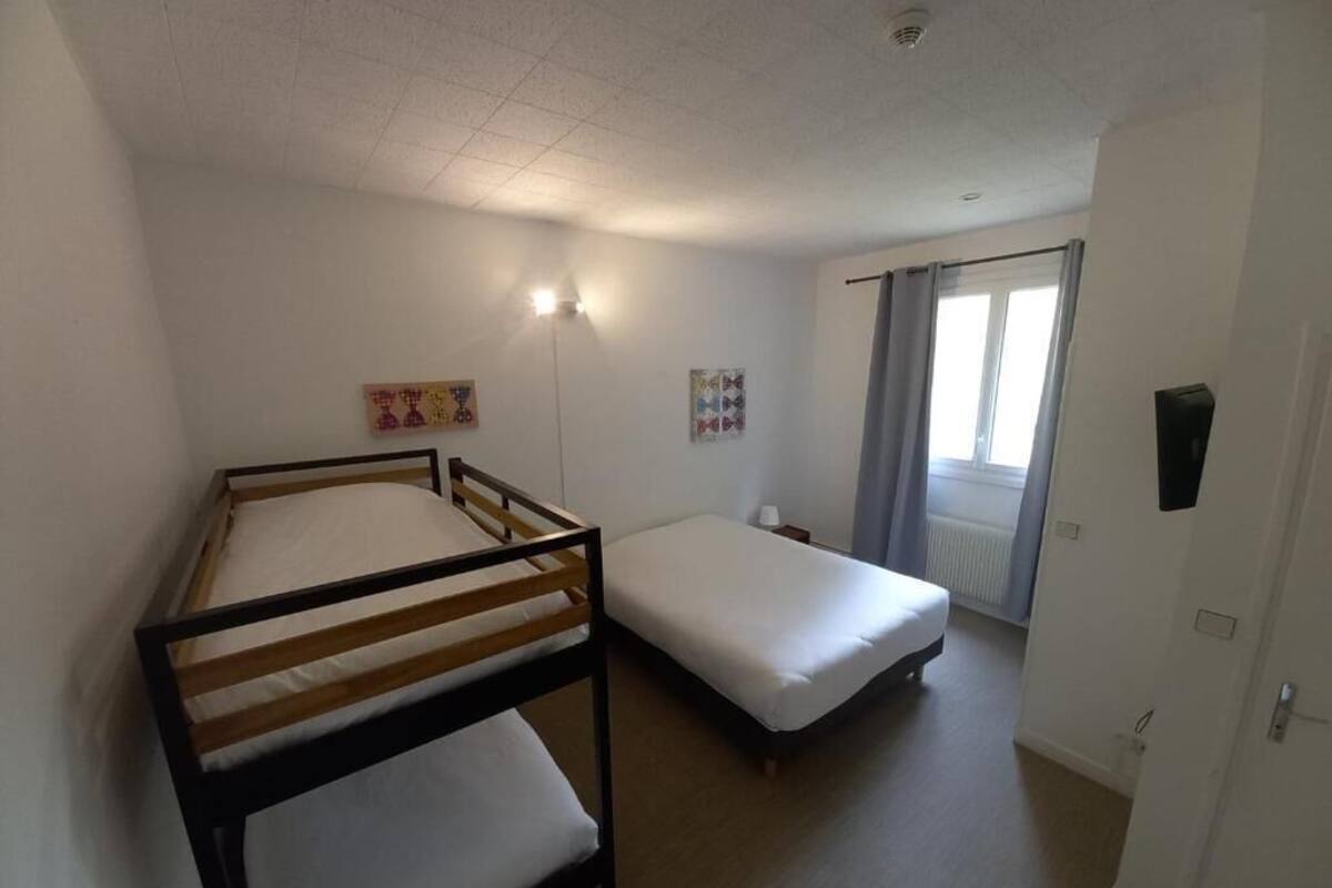 Une chambre avec deux lits simples, une petite table et une fenêtre avec des rideaux.