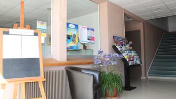 Zona de recepción con mostrador, tablón de anuncios, planta en maceta, estante para revistas y una escalera.
