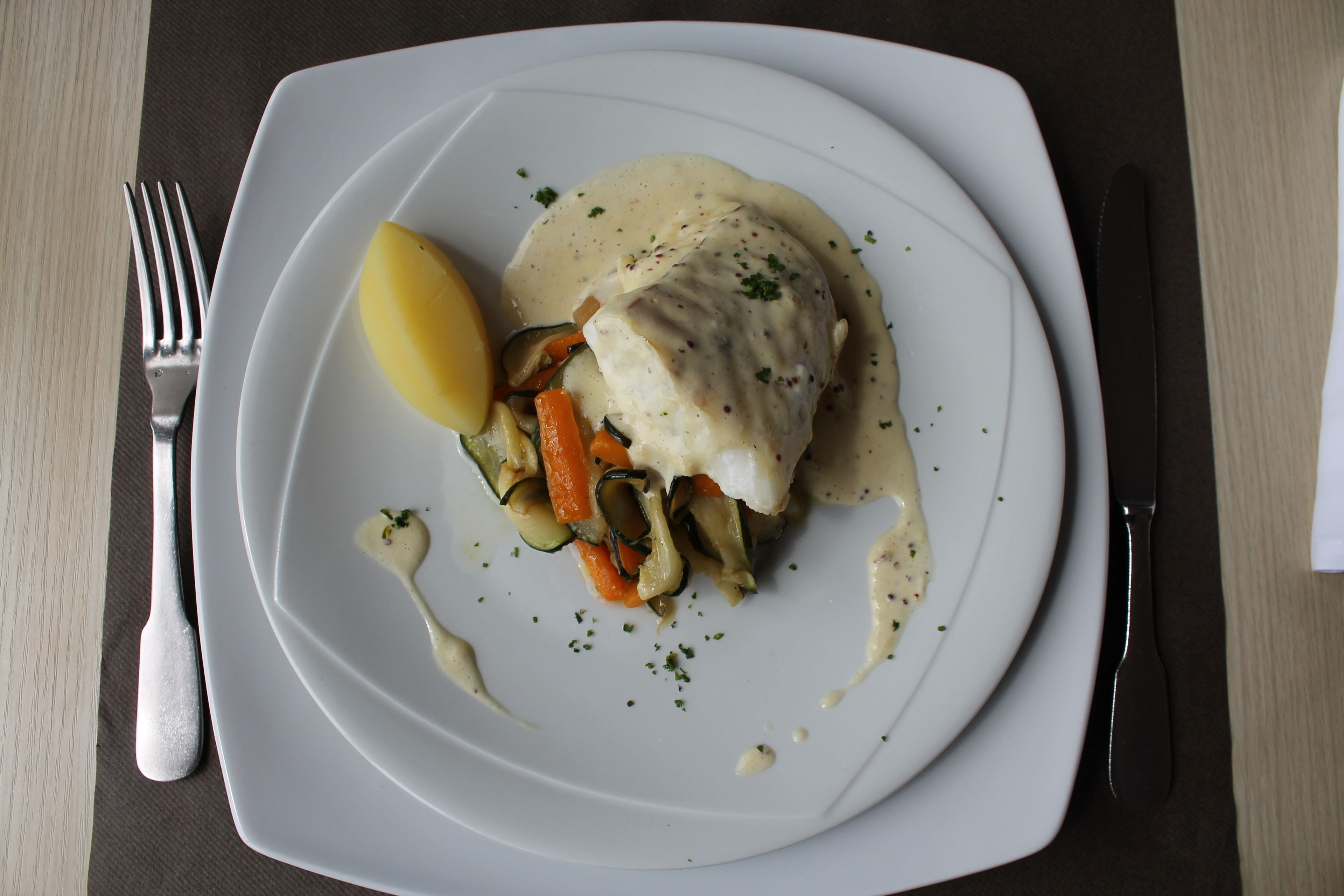 Une assiette blanche contenant un plat de poisson, des légumes et une tranche de citron.