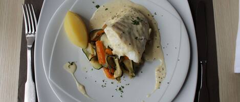 Une assiette blanche contenant un plat de poisson, des légumes et une tranche de citron.