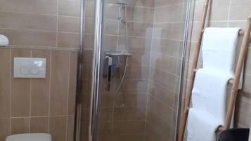 Un espacio de ducha con puerta de vidrio, un inodoro y un perchero con toalla.