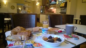 Una mesa de desayuno con cruasanes, pan, un tazón de frutas, yogur y un vaso de jugo.