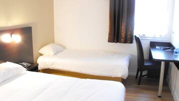 A hotel room with two single beds, a desk with a chair, a telephone, and a window with curtains.