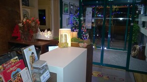Zona de recepción de un hotel con un árbol de Navidad, una lámpara encendida y una exhibición de productos locales.
